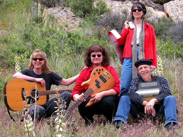 Four band members on a rocky and grassy hillside, holding their instruments.